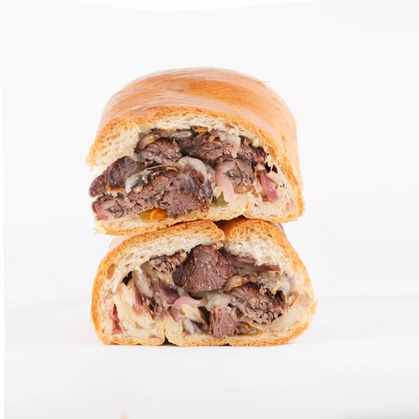 Two halves of a Hollywood Wraps & Grill steak and cheese sandwich, stacked on a white background.