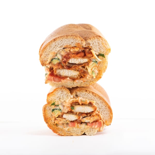 A Hollywood Wraps & Grill fried chicken sandwich, cut in half, revealing crispy chicken, sauce, and vegetables.
