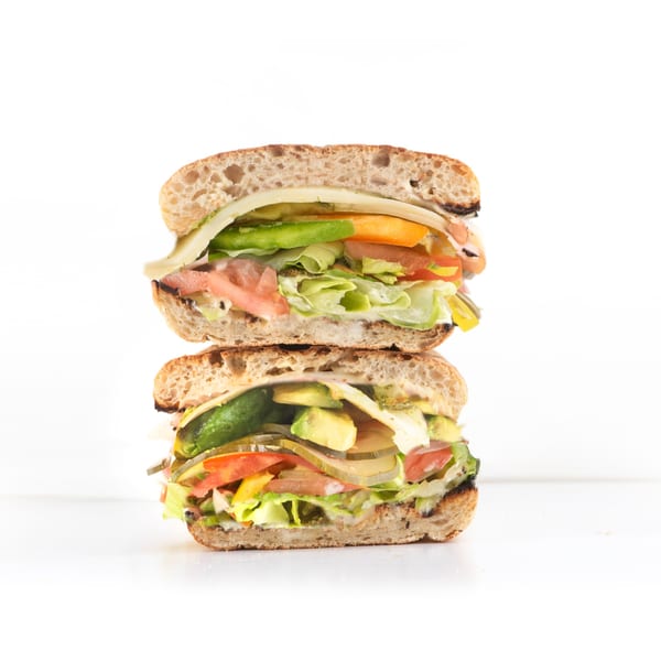 A grilled sandwich, cut in half and stacked, revealing fresh vegetables, cheese, and sauce.